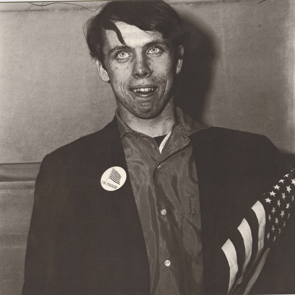 Lot #457: DIANE ARBUS - Patriotic Young Man with a Flag, N.Y.C - Original vintage photogravure